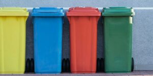 four assorted-color trash bins beside gray wall